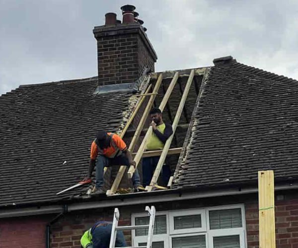 This is a photo of a roof repair being carried out. A section of the roof has been stripped and two roofers are replacing the rafters. Works being carried out by KLJ Roofing Towcester